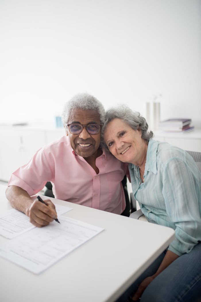 Happy elderly couple sitting at a desk, smiling and signing documents. Perfect for insurance and lifestyle themes.
